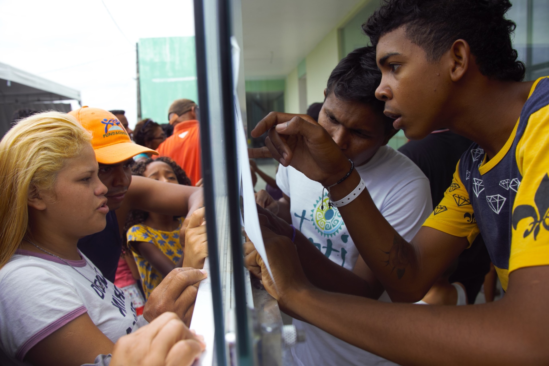 Grupo de venezolanos leyendo lista a través del vidrio