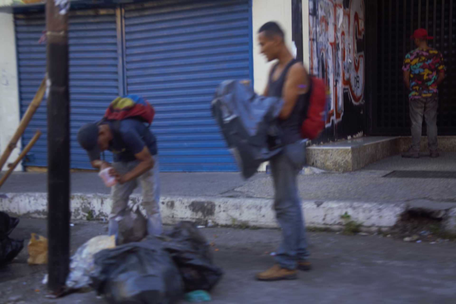 Hombres con mochilas hurgando en la basura en una esquina