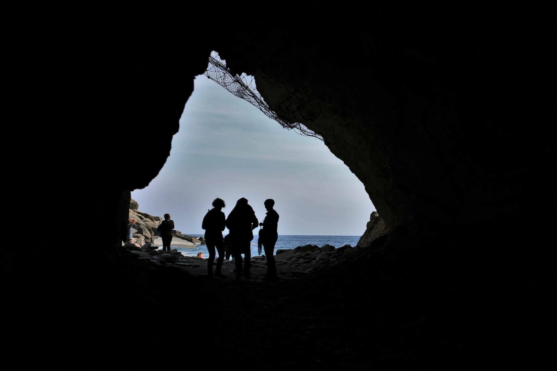 Siluetas a contraluz dentro de una cueva frente al mar