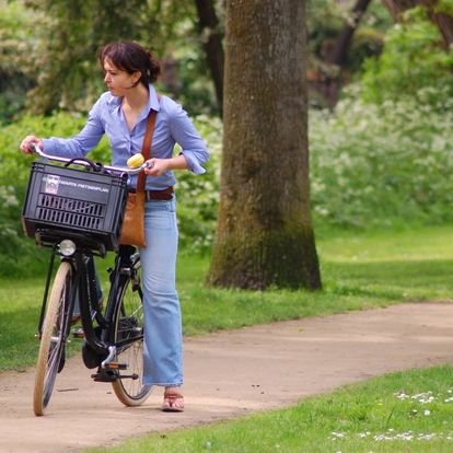 Mujer caminando con bicicleta en parque arbolado