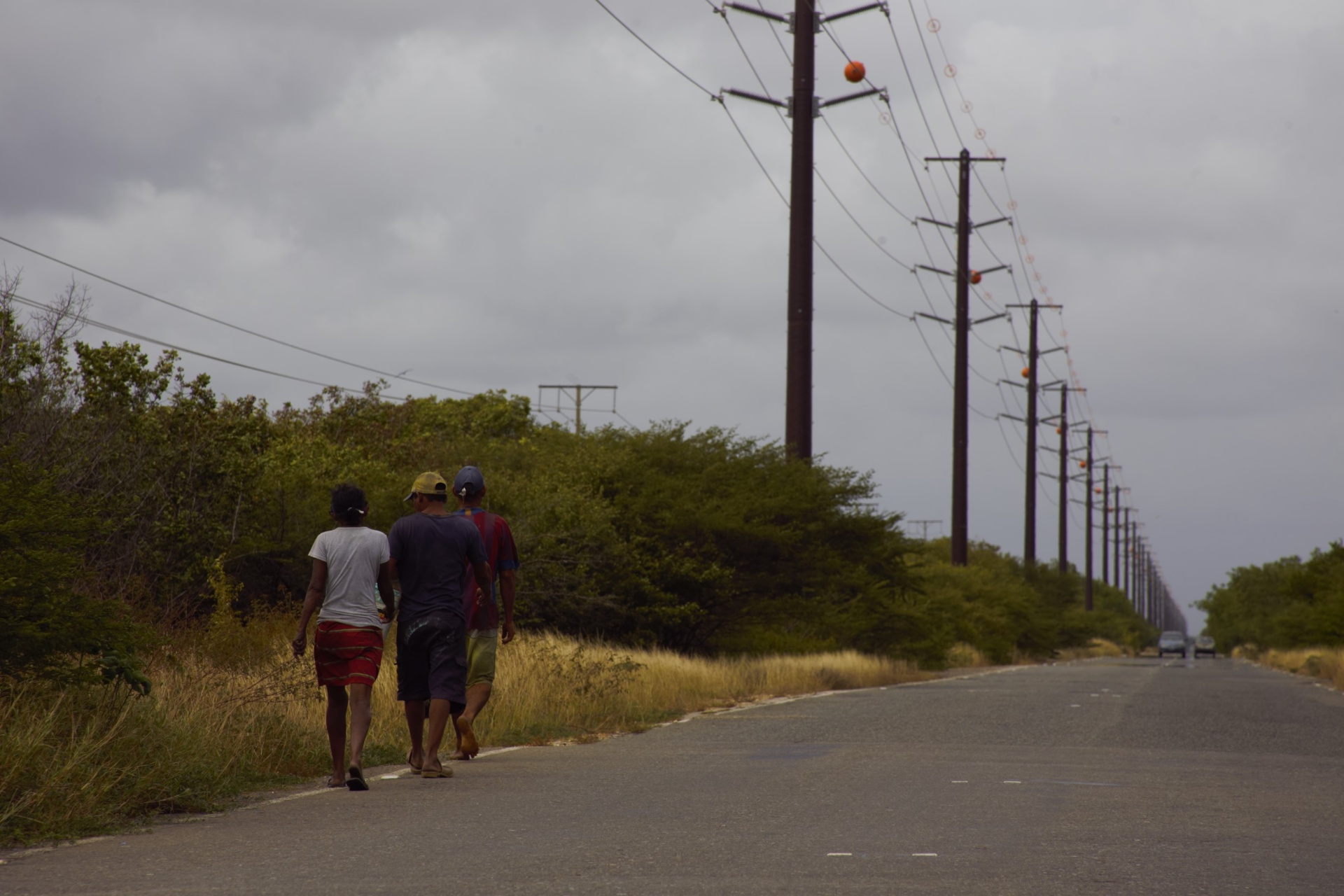 Tres caminantes venezolanos por la carretera bajo cielo nublado