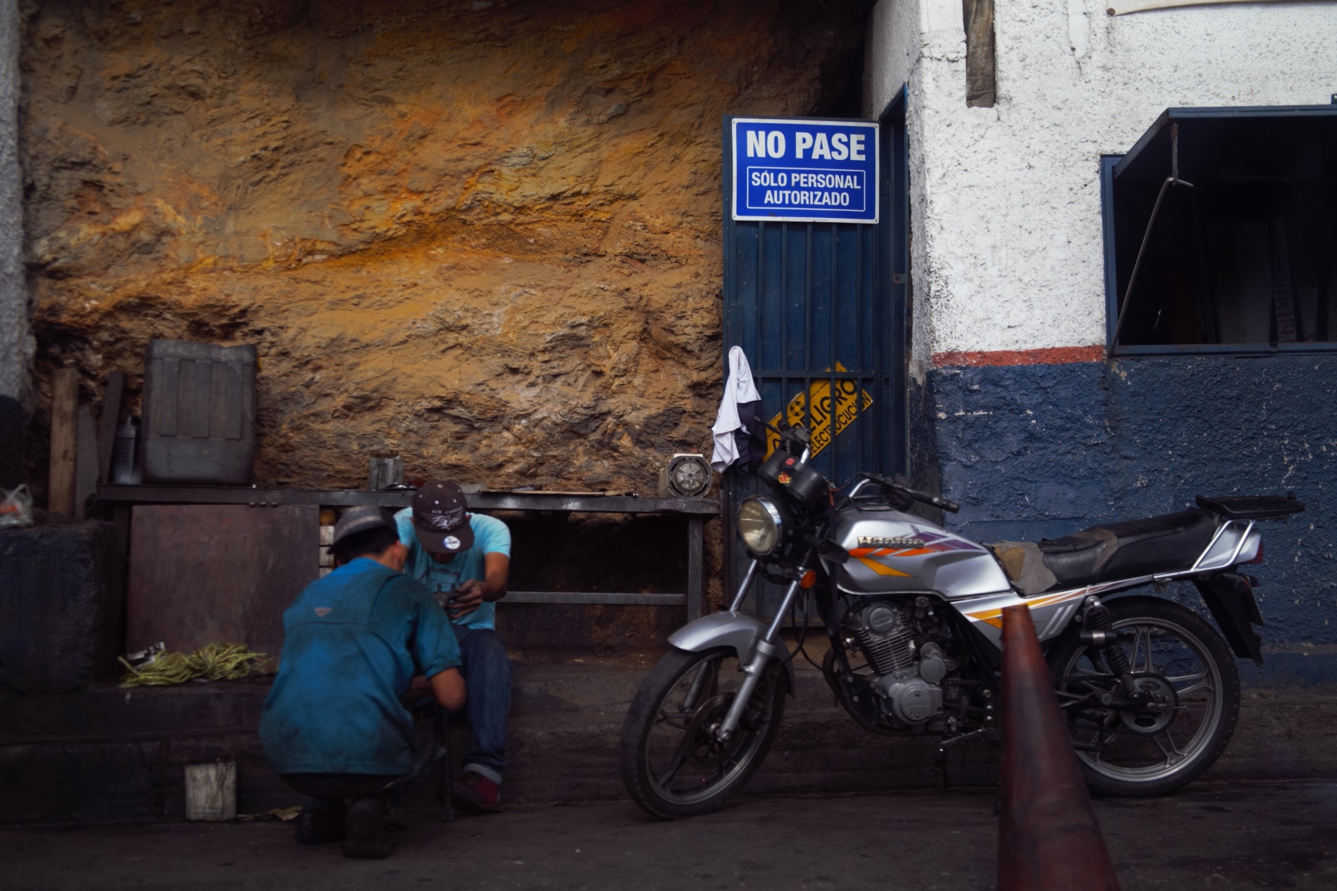 Mecánicos trabajando junto a una moto bajo cartel 'No Pase'